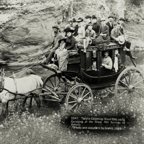 A large group of people ride in and on top of a stagecoach, Hot Springs, South Dakota, 1889.