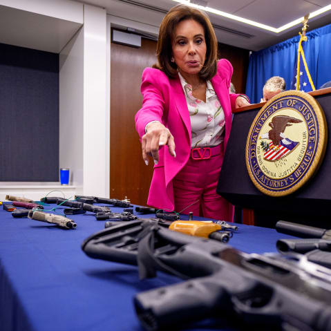 Jeanine Pirro, left, points to a table of guns in front of her.