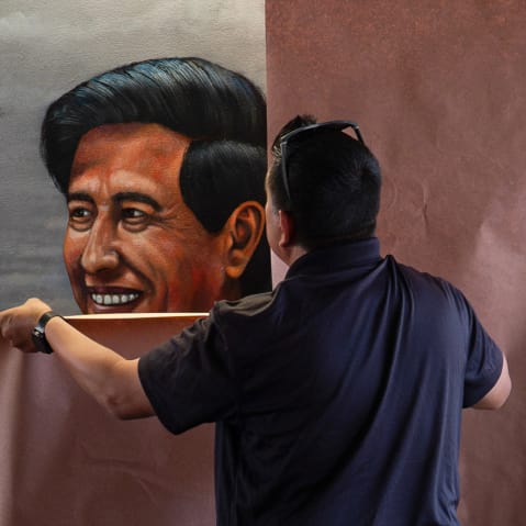 A person puts brown paper on top of a mural featuring Cesar Chavez.
