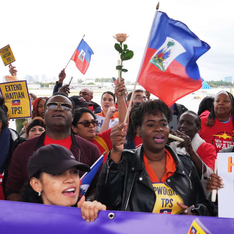 A crowd of people wave Haitian flags and hold signs calling for an extension to Haitian TPS.