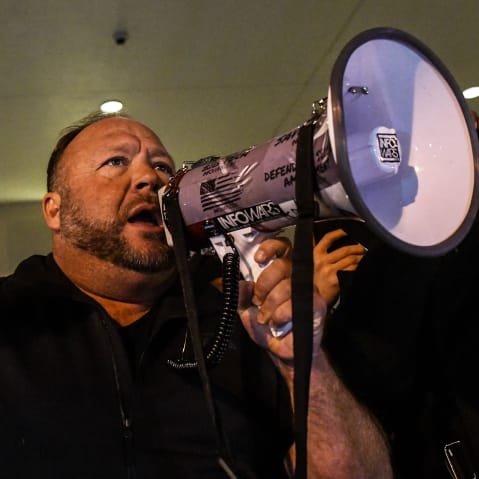 Alex Jones has one fist raised and holds a megaphone with the other hand.