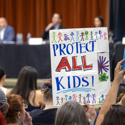An attendee holds a sign that reads "Protet All Kids" seen from behind.