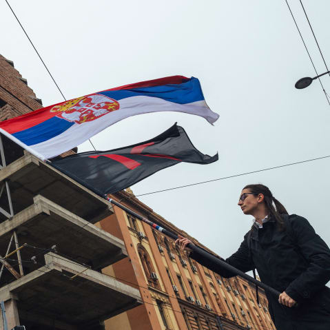 A demonstrator waves the Serbian flag in in Belgrade, Serbia, in front of a run-down building.