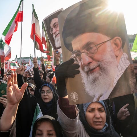 People wave Iranian flags and carry portraits of Ayatollah Ali Khamenei.