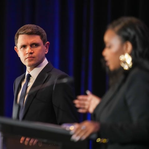 James Talarico, in focus, left, looks at Jasmine Crockett, out of focus, right, as she speaks. Both stand at podiums with microphones.