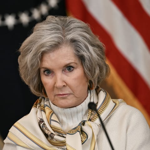 Susie Wiles sits during a meeting, wearing a beige sweater and a scarf around her neck.
