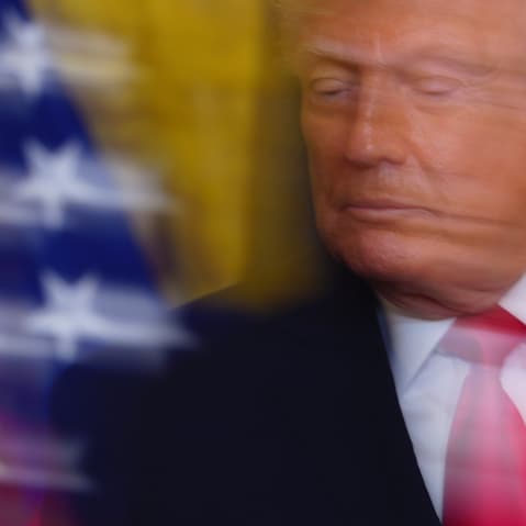 A photo of Donald Trump taken with a slow shutter speed. Part of an American flag is visible on the left-hand side of the photo.