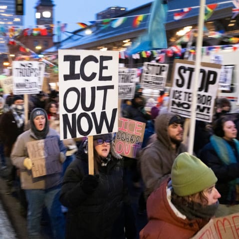 People holding picket signs against ICE march in the street.