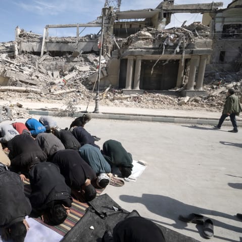 Men put their faces on the ground as they pray outside the ruins of a building.