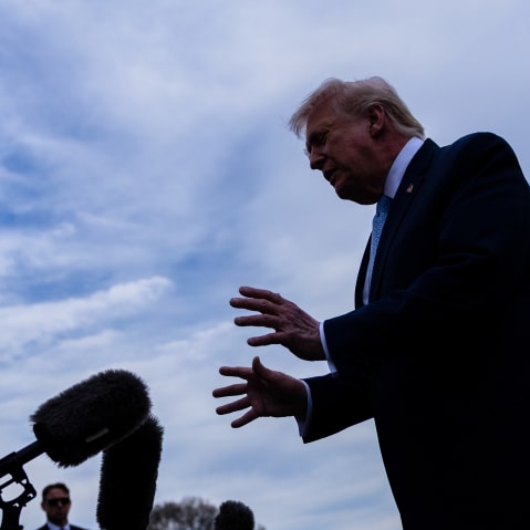 In this photo shot from below, journalists with mics and recorders can be seen on the left as Donald Trump speaks to them as he makes a gesture with his hands.