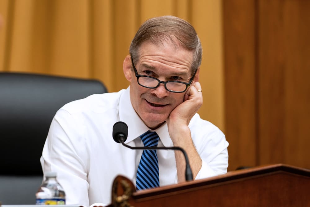 Jim Jordan, right, rests his head on his hand as he talks to a person turned away from the camera.