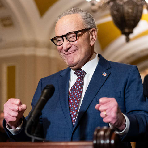 Chuck Schumer pumps his fists in excitement behind a podium.