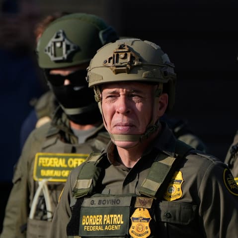 Greg Bovino, center, squints in the light beside multiple federal immigration agents.