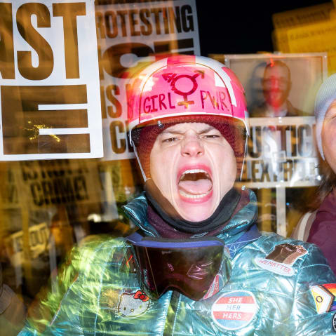 A person with their mouth open holds a picket sign at a protest.