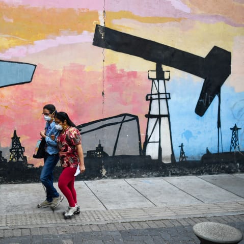 Women walk past a mural depicting an oil pump on April 14, 2021 in a street of Caracas, Venezuela.