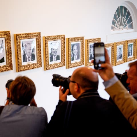 Members of the media take photographs of framed portraits part of the "Presidential Walk of Fame" on the wall of the colonnade outside the Oval Office.