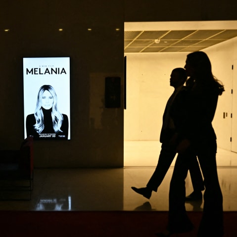 Silhouettes walk past a poster for "Melania."