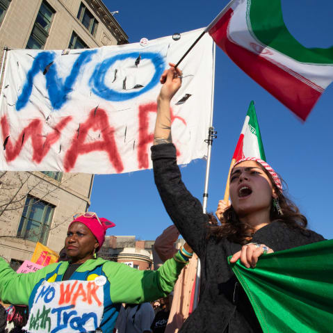 People wave Iranian flags and hold signs that say "NO WAR" and "NO WAR with Iran."