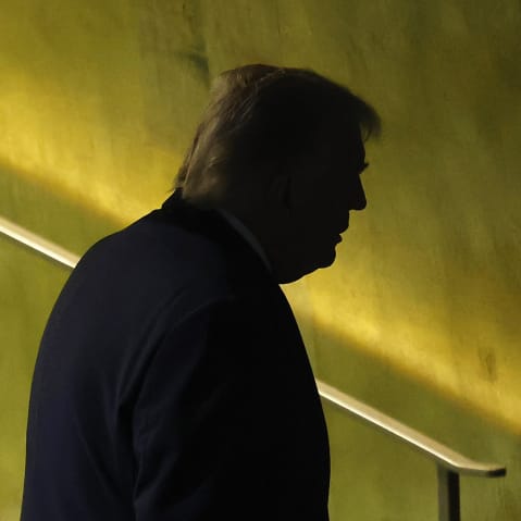 Donald Trump's darkened profile is seen as he walks away in front of a yellowish green background.