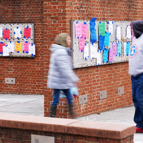 One person looks at posted signs while two others walk by explanatory panels that were part of an exhibit on slavery at President's House Site.