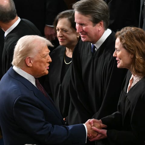 Donald Trump shakes Amy Coney Barrett's hand. They are surrounded by other Supreme Court justices.