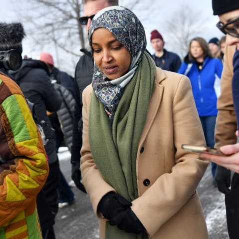 Ilhan Omar talks to a reporter as she walks on the street in winter.