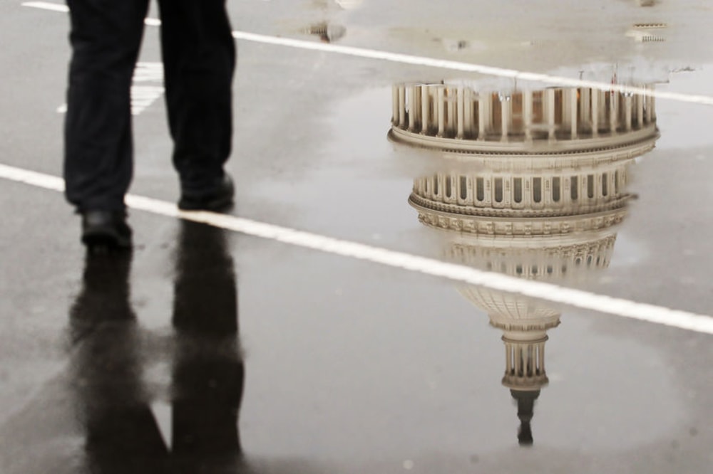 The dome of the U.S. Capitol Building is reflected in a puddle on a rainy morning in Washington