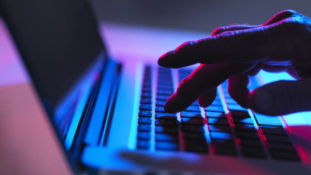 Image: Silhouette of male hand typing on laptop keyboard at night