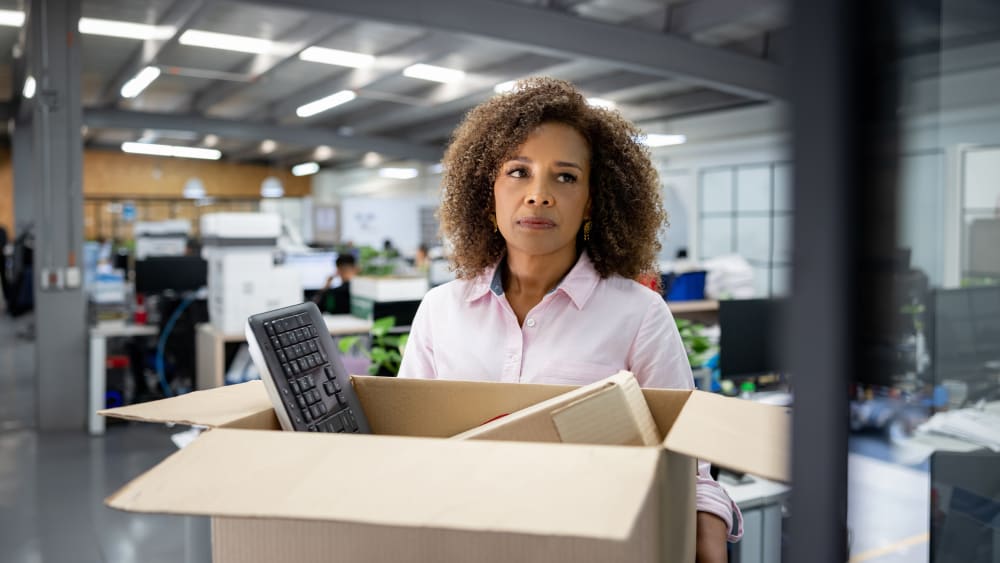 Business woman being fired from her office and carrying a box with her belongings