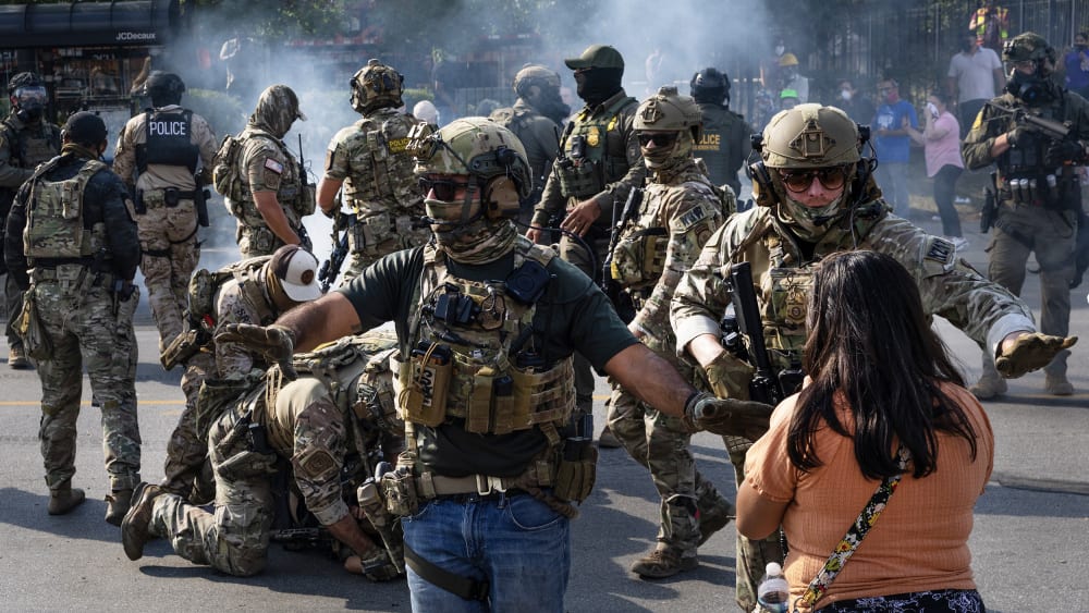 Police take two people into custody, as tear gas fills the air after it was used by federal law enforcement agents in Broadview, IL.