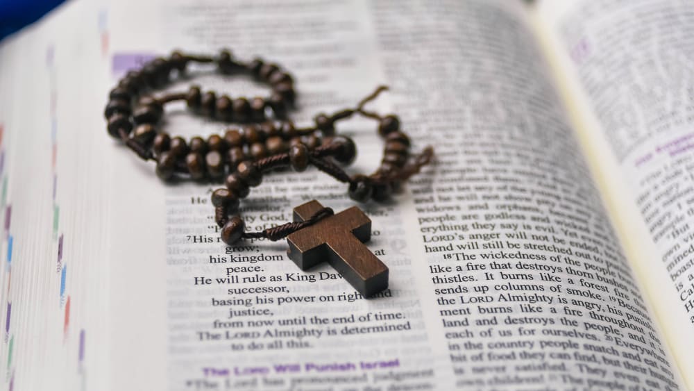 Table top view of a wooden rosary resting on a Bible.