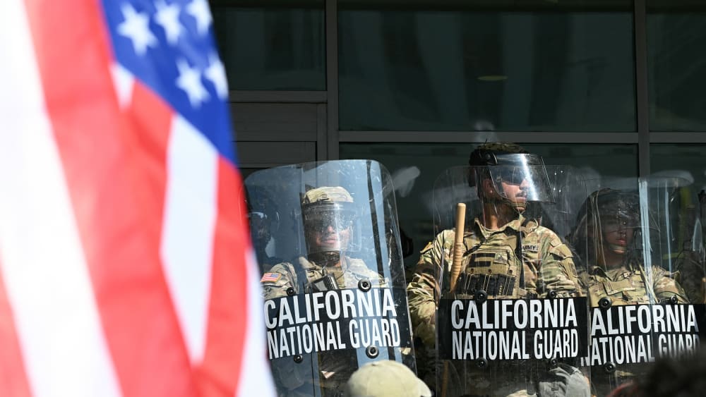 A demonstrator holds an upside down US flag as they face California National Guard.