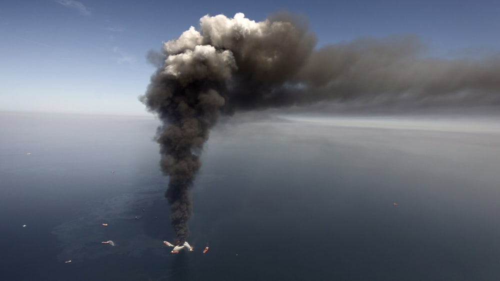In this Wednesday, April 21, 2010 file photo, oil can be seen in the Gulf of Mexico, more than 50 miles southeast of Venice on Louisiana's tip, as a large plume of smoke rises from fires on BP's Deepwater Horizon offshore oil rig.