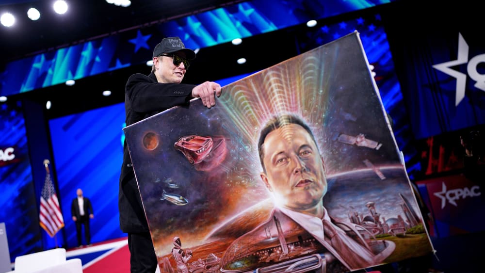 Elon Musk holds a painting of himself.