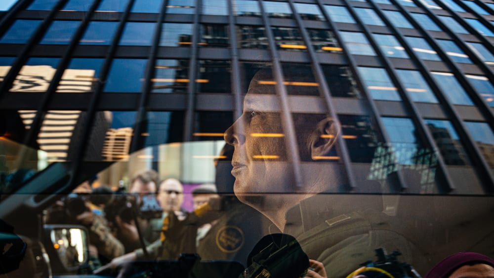 U.S. Border Patrol commander Gregory Bovino sits in the driver's seat surrounded by media and protesters.