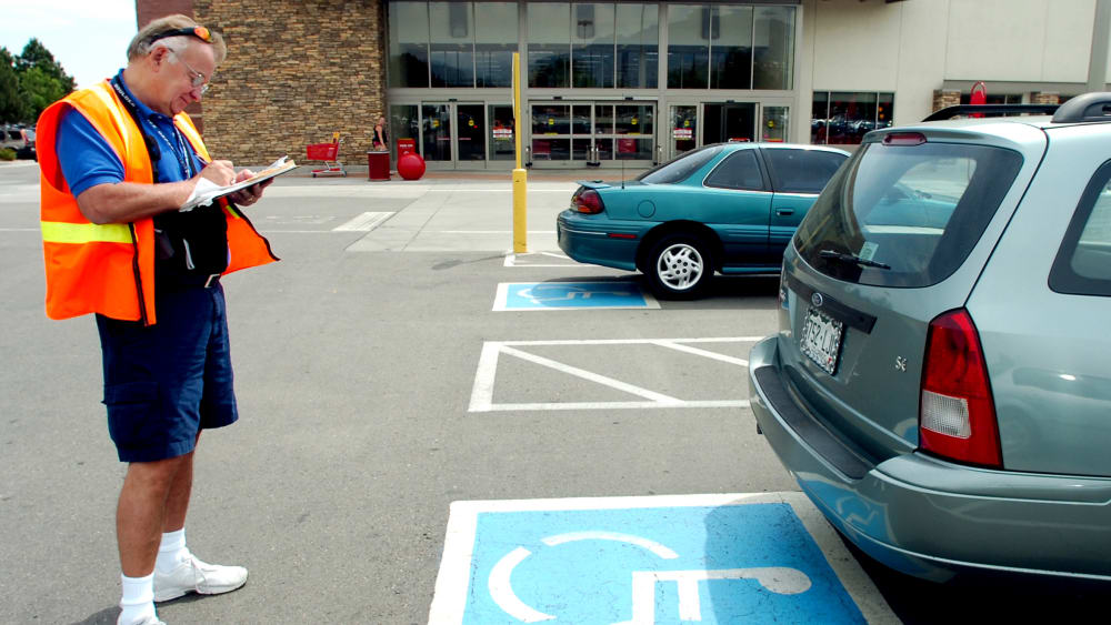 Volunteer handicapped parking enforcement officer writes a parking ticket for a car parked without a handicapped plate or place card.