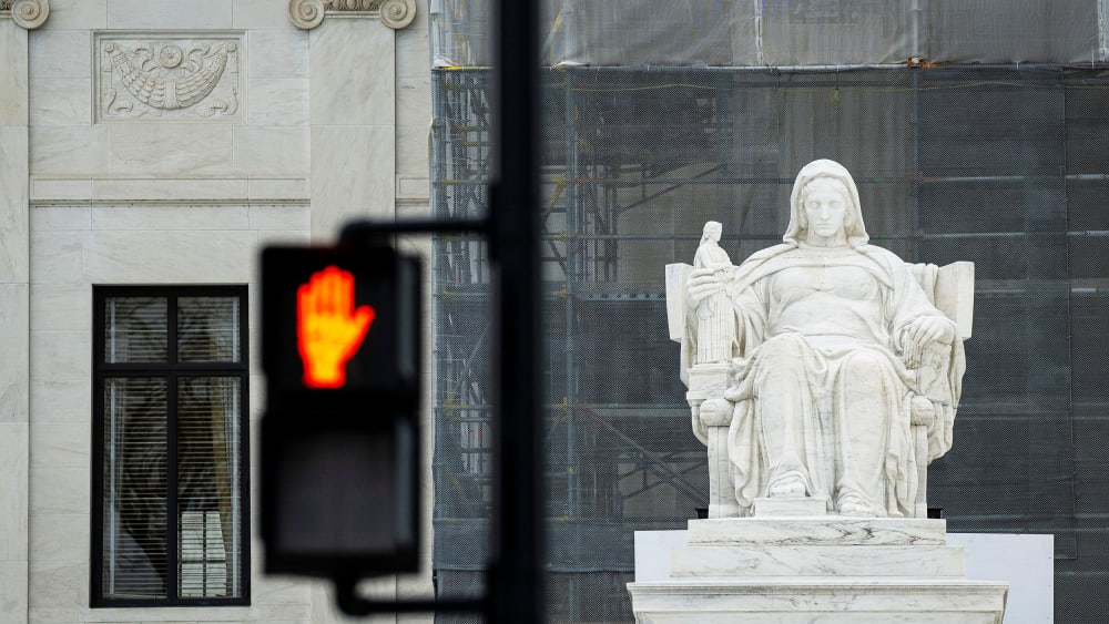 The Contemplation of Justice statue outside the US Supreme Court beside a "Don't Walk" upraised hand symbol in Washington, D.C.