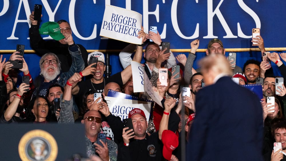 An attendee holds a "Bigger Paychecks" sign during an event on inflation with US President Donald Trump.