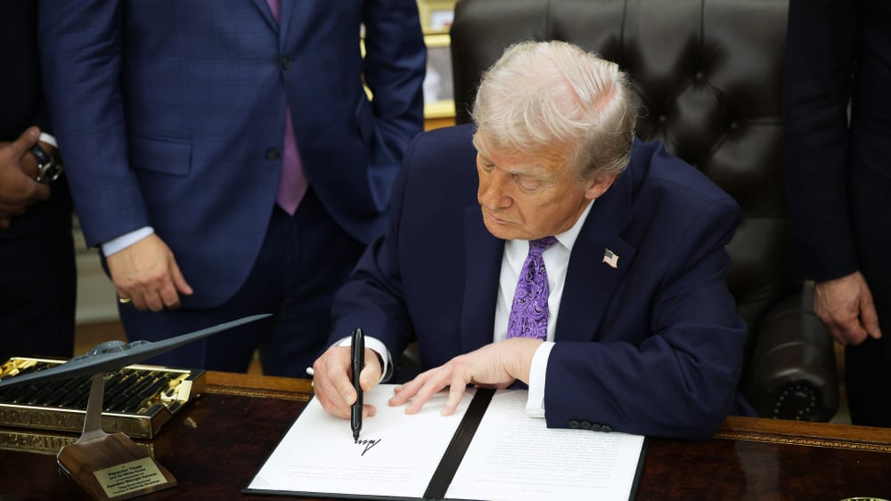 President Donald Trump signs an executive order in the Oval Office.