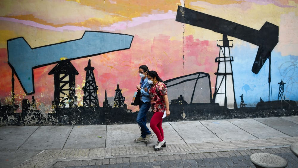 Women walk past a mural depicting an oil pump on April 14, 2021 in a street of Caracas, Venezuela.