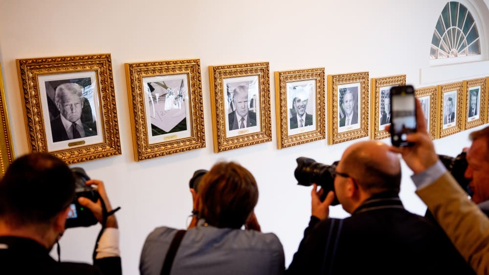 Members of the media take photographs of framed portraits part of the "Presidential Walk of Fame" on the wall of the colonnade outside the Oval Office.