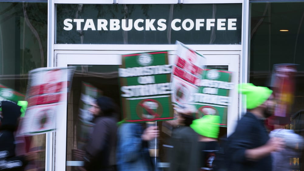 People blurred in motion hold signs in front of a Starbucks Coffee location.