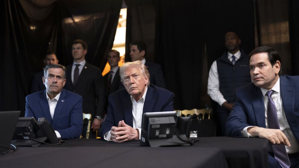 President Donald Trump, center, sits with his hands folded.