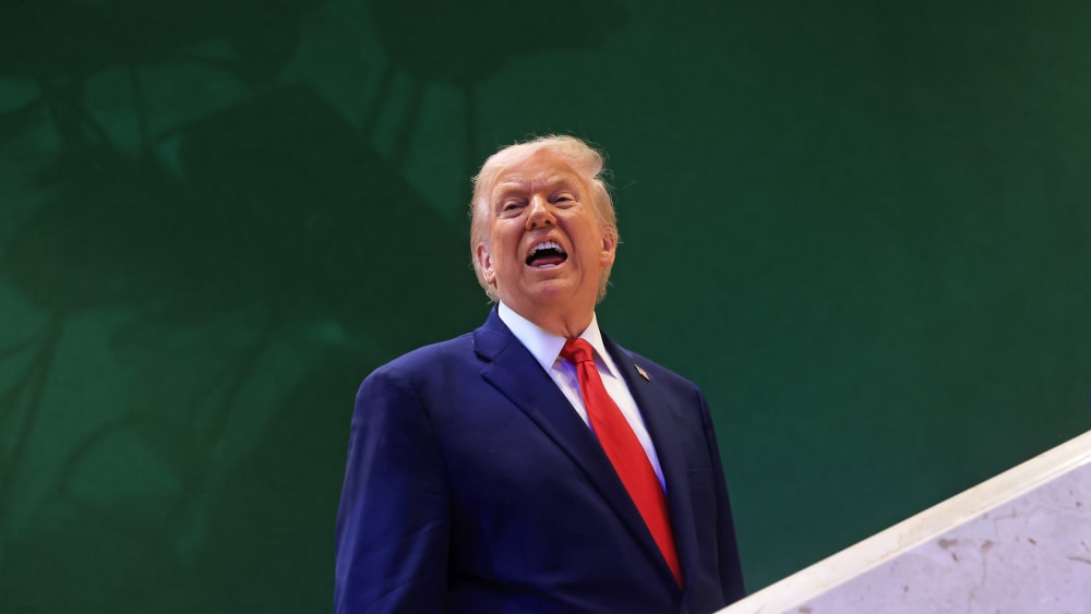 Donald Trump against a green wall, with his mouth open.