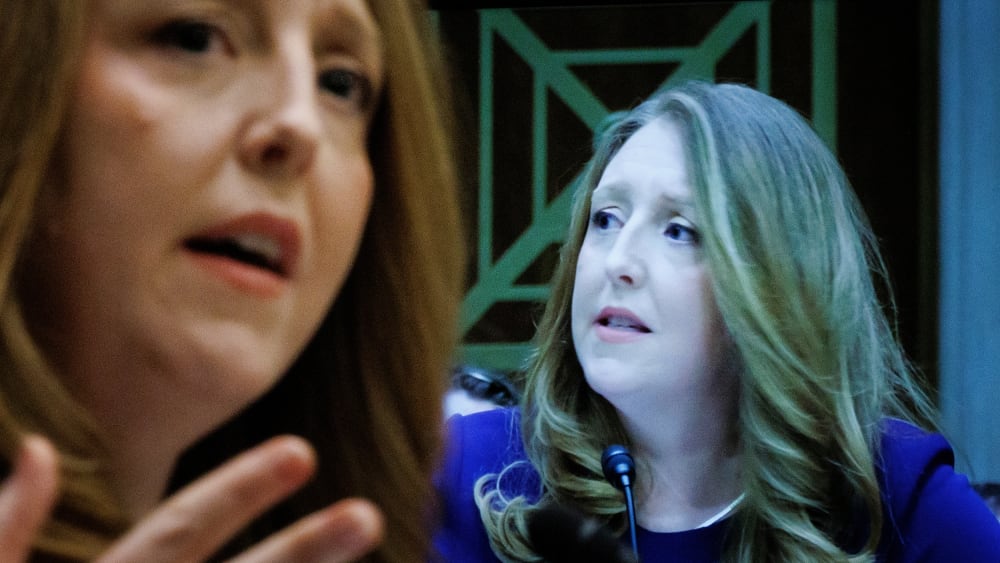 Casey Means in seen out of focus on the left side of the frame while her face is shown on a screen on the right - in focus.