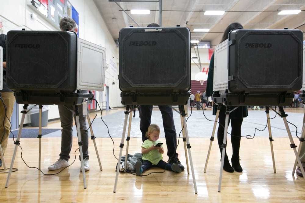 Image: A child waits between her father's legs as he and other voters cast their ballots for the mid-term elections
