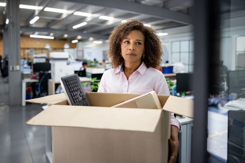 Business woman being fired from her office and carrying a box with her belongings