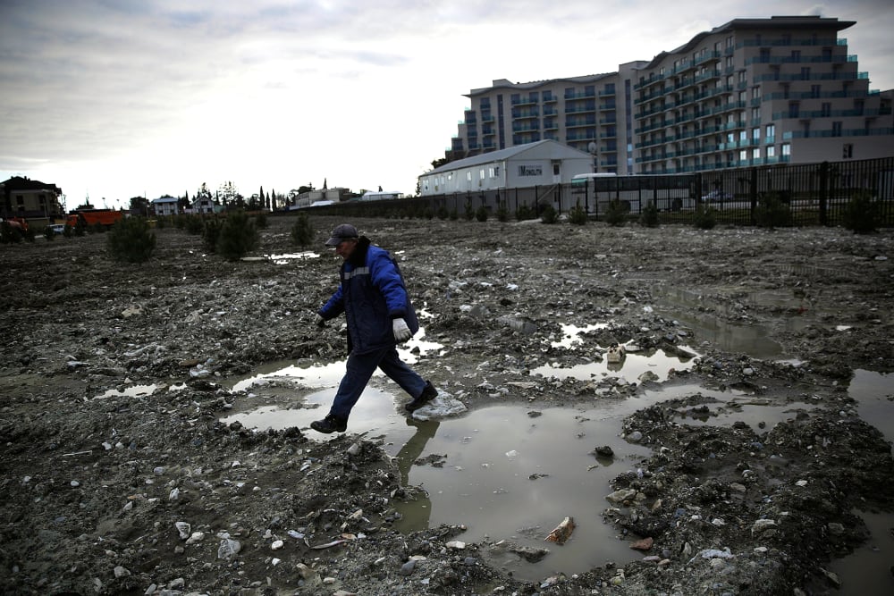 A construction worker steps over a puddle in a lot being prepared to be turned into a grassy lawn on Feb. 6, 2014, in Sochi, Russia.