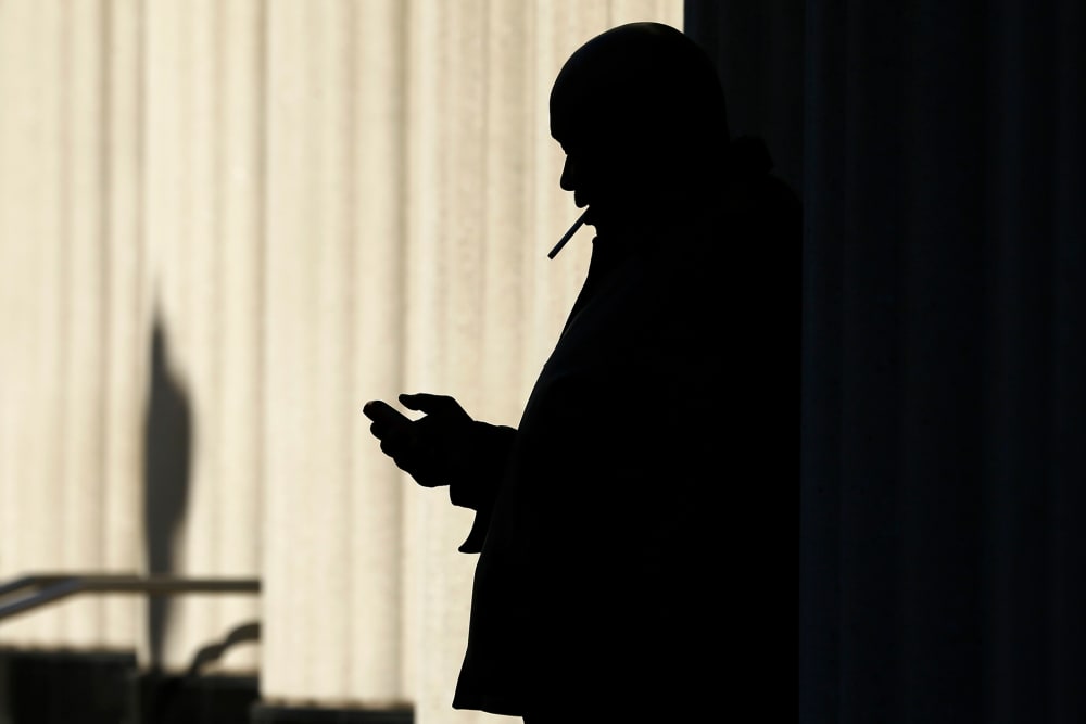 A man on his mobile phone as he smokes a cigarette outside, Dec. 9. 2013, in San Diego, Calif.