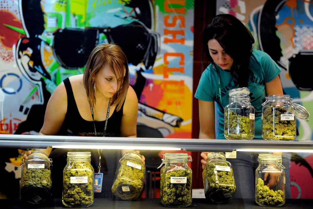 Brittany Zewe, left, and Jess Vanderpool take jars of different strains of marijuana off the counter between customers at Denver Kush Club in Denver, Colorado on Jan. 1, 2014.